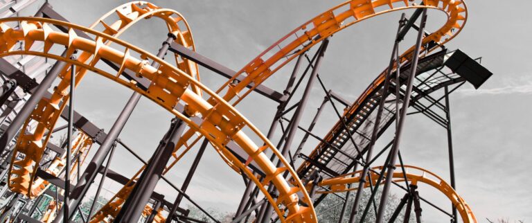 Orange Achterbahn mit verschlungenen Schienen vor bewölktem Himmel