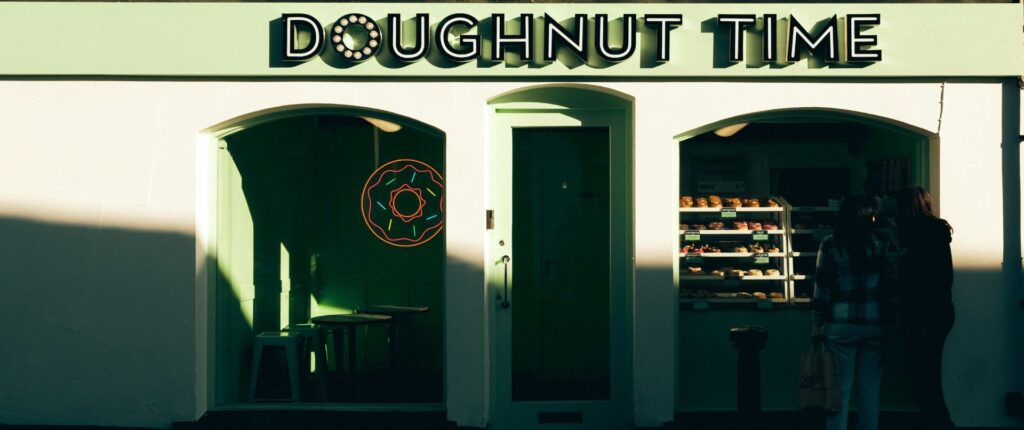 Zwei Personen stehen vor dem Schaufenster eines Donat-Geschäftes und schauen in die Auslage