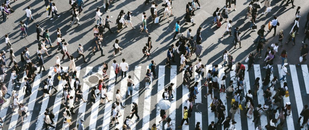 Eine große Strasse mit einem Zebrastreifen über den sehr viele Menschen gehen, von oben betrachtet